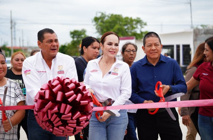 A ribbon-cutting ceremony outdoors with a woman in a white shirt cutting a pink ribbon, surrounded by people holding scissors and watching.