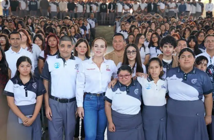 Group of students and staff posing for a photo outdoors, centered on a woman in a white shirt and jeans with others in uniform around her.