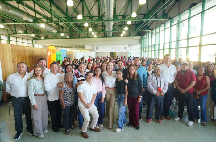 Large diverse group of people posing for a group photo inside a bright hall at a community event.