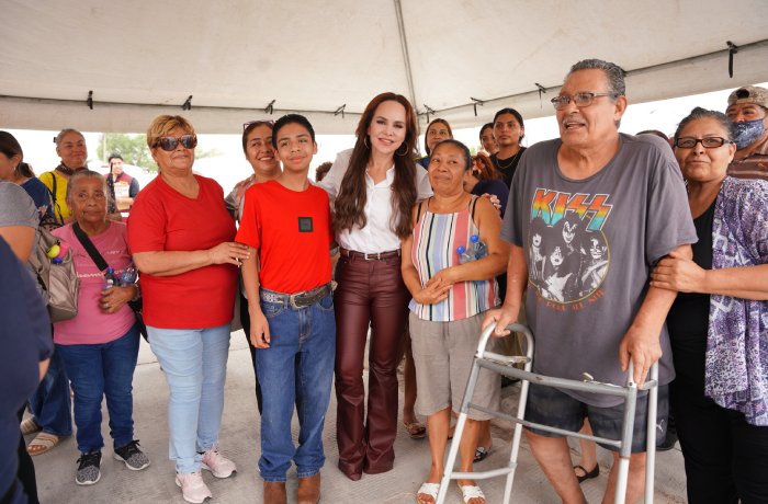 Multicultural group posing under a canopy with a woman in a white top and maroon pants at a community event.