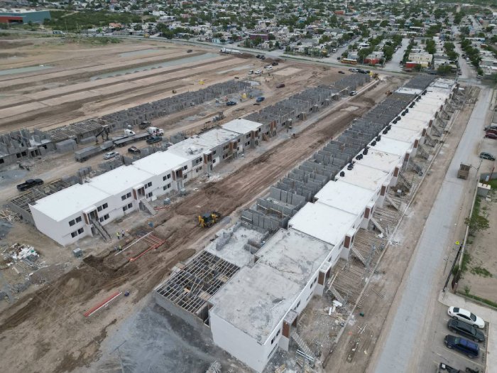 Aerial view of a new housing development with long rows of white apartment blocks under construction and heavy machinery nearby.