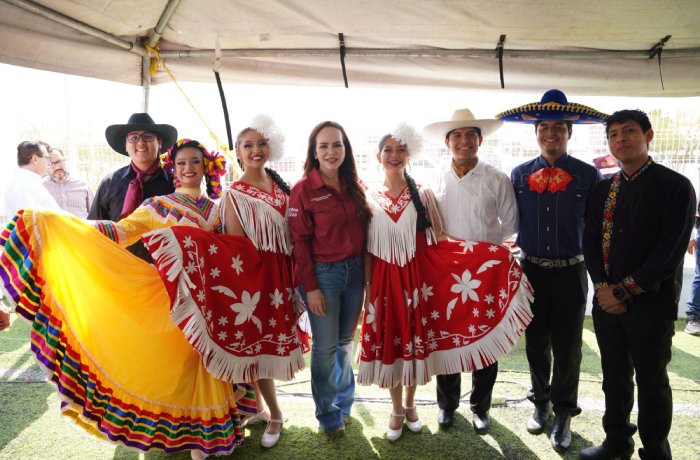 Group of performers under a canopy; women in bright red and white fringed folk dresses, men in traditional outfits with hats.