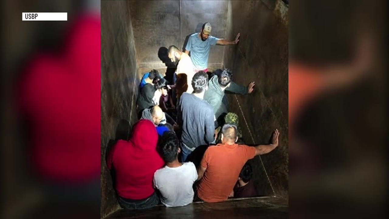 Crowd of people packed into a narrow vertical shaft, some touching the walls as they await rescue, with one man at the top supervising.