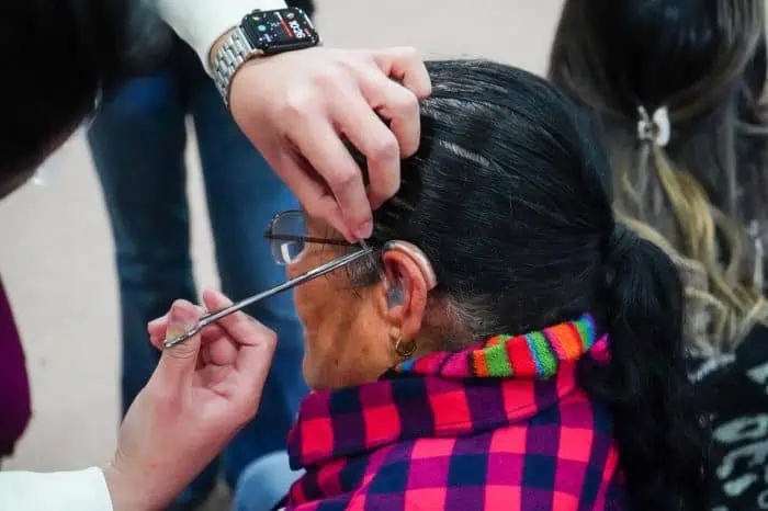 Caregiver helps an elderly woman adjust her glasses, guiding the temple by her ear.