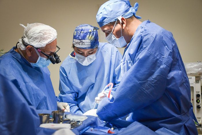 A surgical team in blue gowns, masks, and caps performing an operation in a sterile operating room.