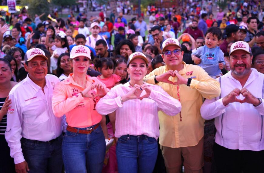 Group of people in a crowd forming heart shapes with their hands, smiling at the camera during an outdoor event.