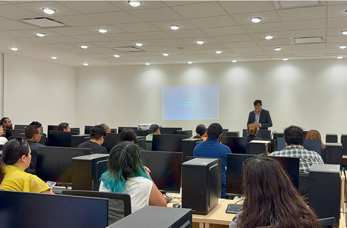 Instructor presenting at the front of a computer lab as adult students sit at desks with desktop PCs.
