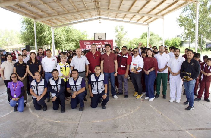 Group of people posing under a pavilion on an outdoor basketball court; several wear uniforms, banner visible in the background.