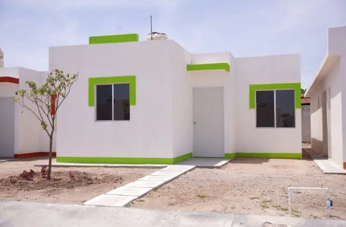 Front view of a white modern house with lime green trim, a central door, two front windows, and a concrete walkway. Dry yard with a small tree on the left.