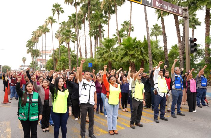Group of diverse people in a street protest raising fists, some wearing safety vests, with palm trees in the background.
