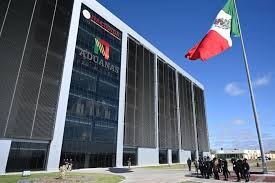 Exterior of a modern Mexican political party headquarters with a DEMÓCRATAS sign, glass facade, and a tall Mexican flag nearby.