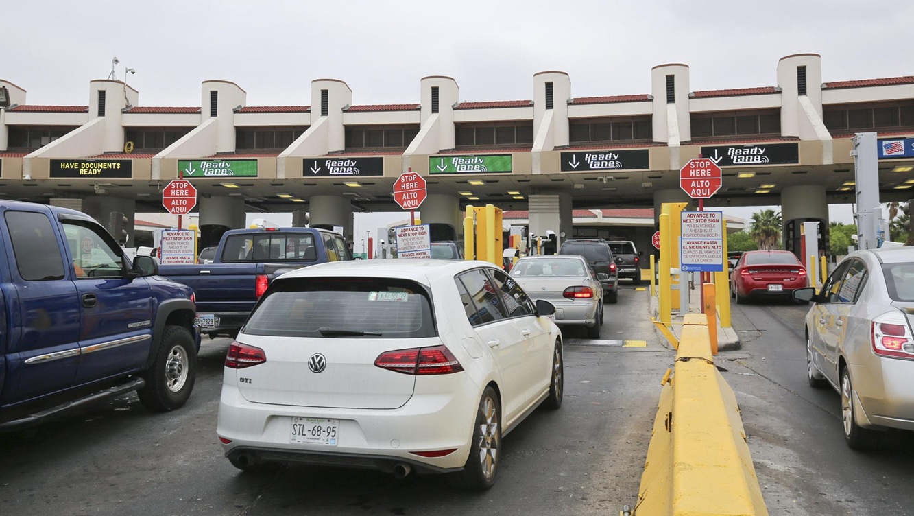 Cars line up at a toll plaza with yellow barriers and 'Ready lanes' signs above the booths; a white VW GTI is closest to the camera on the left side of the lane.
