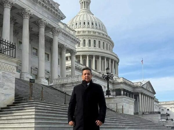 Man in a black coat stands on the marble steps in front of the U.S. Capitol building.
