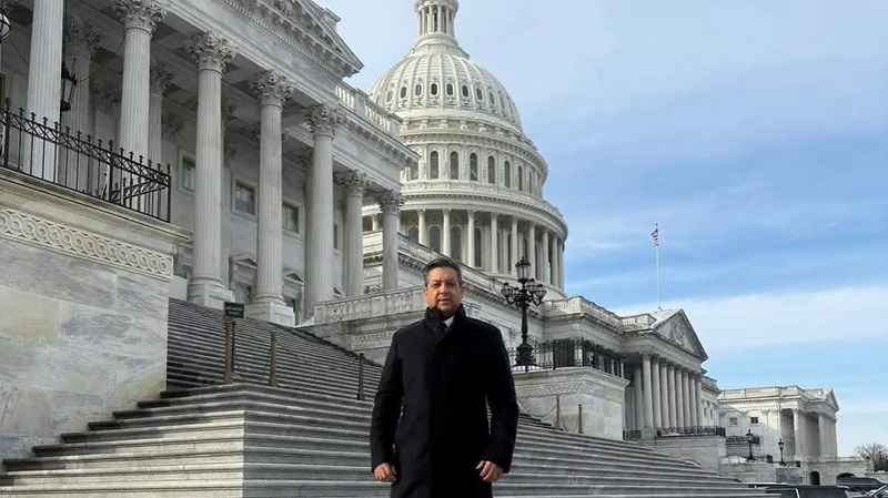 Man in a black coat stands on the marble steps in front of the U.S. Capitol building.
