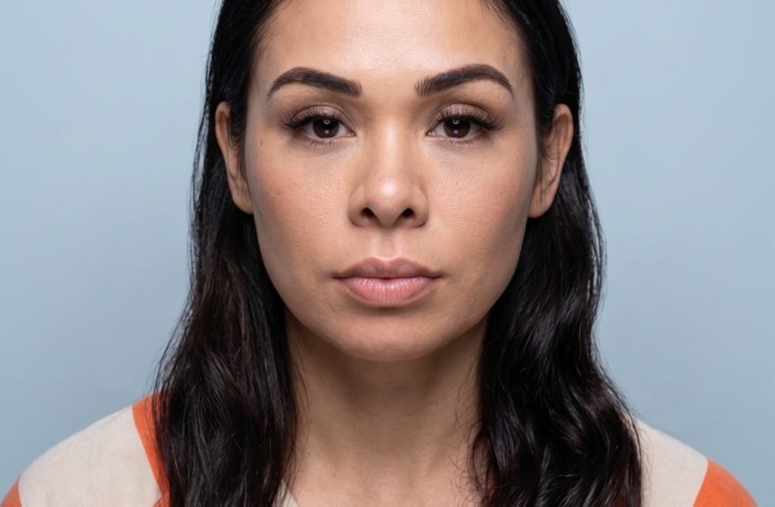 Close-up of a woman's face from the eyebrows to chin, with dark hair and an orange-and-beige striped shirt against a blue background.