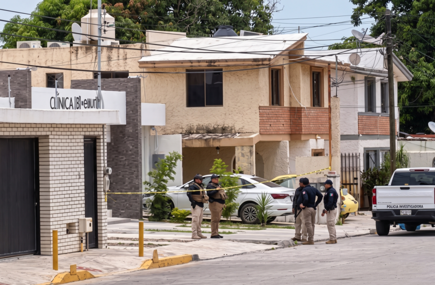 Group of police officers standing on a residential street near a crime scene with yellow tape and a white investigation pickup in the background.