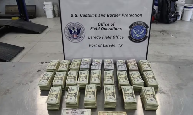 Stacks of bundled cash laid out on a table with a U.S. Customs sign in the background (Port of Laredo, TX).