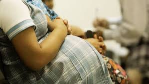 Pregnant person sitting with a partner's hands gently resting on their baby bump.