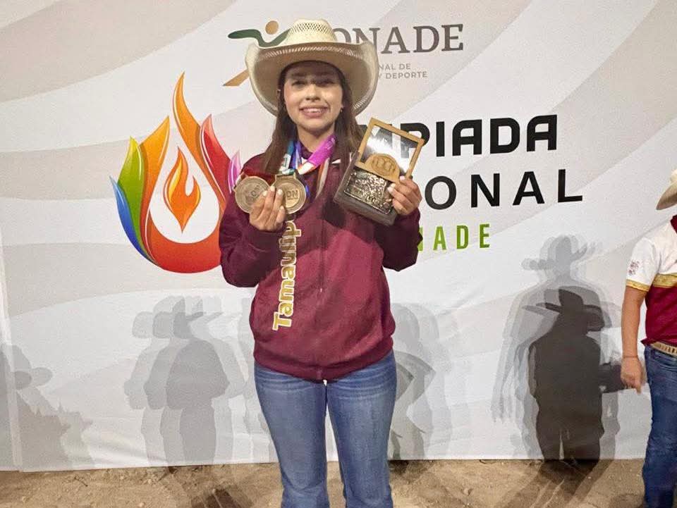 Young woman wearing a cowboy hat shows her medals and a trophy on stage at a sports award event.
