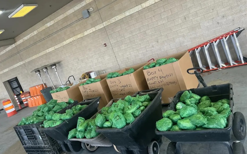Loading bay with black carts full of green bags and cardboard boxes labeled Box 2–4 nearby a red ladder.
