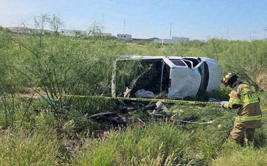 White van overturned on its side in tall grass, firefighters and yellow caution tape nearby