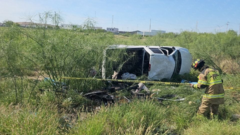 White van overturned on its side in tall grass, firefighters and yellow caution tape nearby