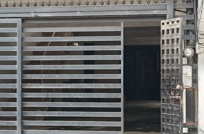 Industrial metal gate with horizontal slats partially open, revealing a dark interior doorway and a utility meter on the right.