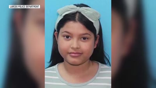 Young girl wearing a light-colored headband and a striped gray shirt, against a blue background; Laredo Police Department watermark in the corner.
