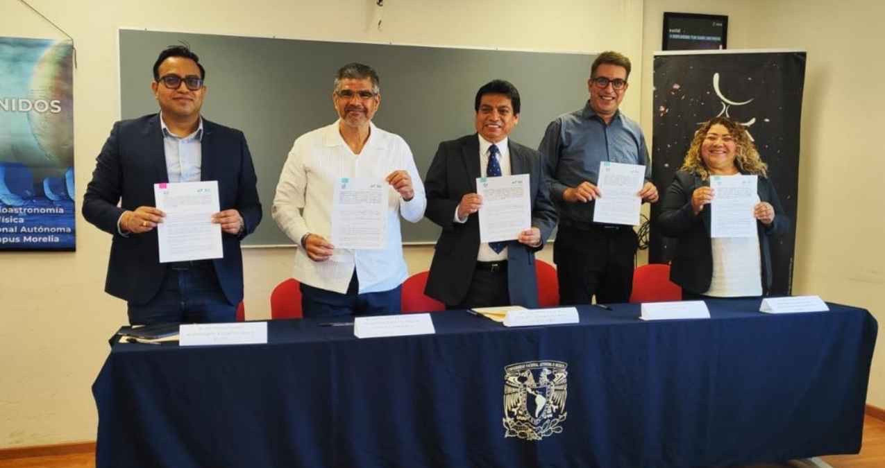 Five professionals in business attire stand behind a table, each holding signed documents during a formal signing ceremony.
