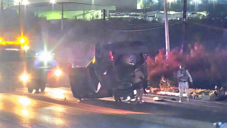 Overturned vehicle on a street at night with flashing emergency lights and responders tending the scene.